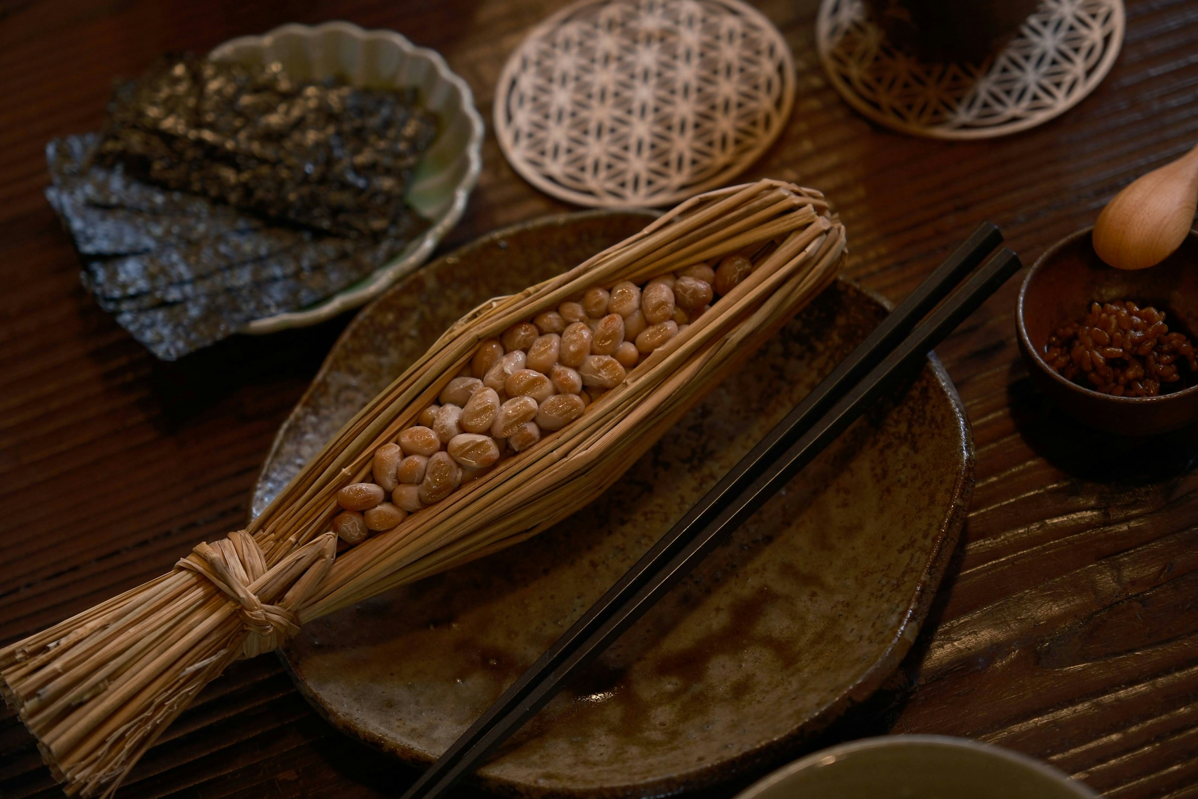 Natto in a straw wrapping, nori and ceramic dishes on a traditional wooden table